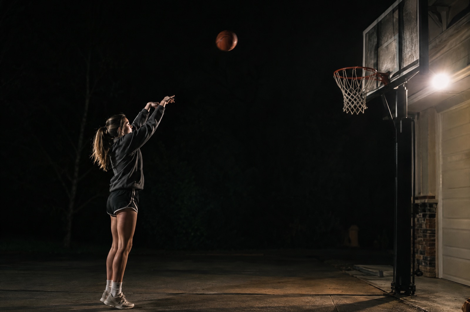 Girl shooting a free throw at a driveway hoop at night
