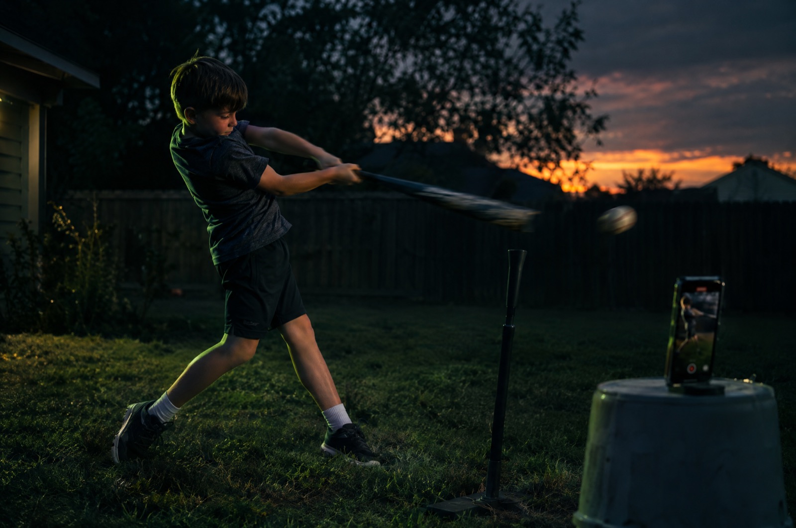 Boy swinging a bat off a tee while a propped phone counts
